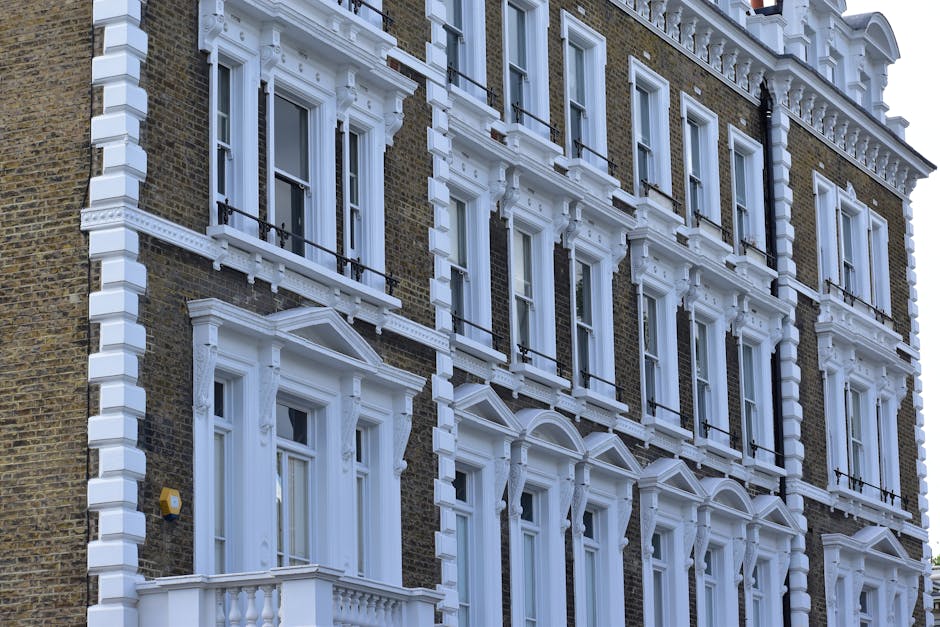 A row of Victorian-style terraced houses with multi-colored facades in pastel tones, including blue, pink, and cream, featuring white decorative trim around the bay windows and doors. The houses are c